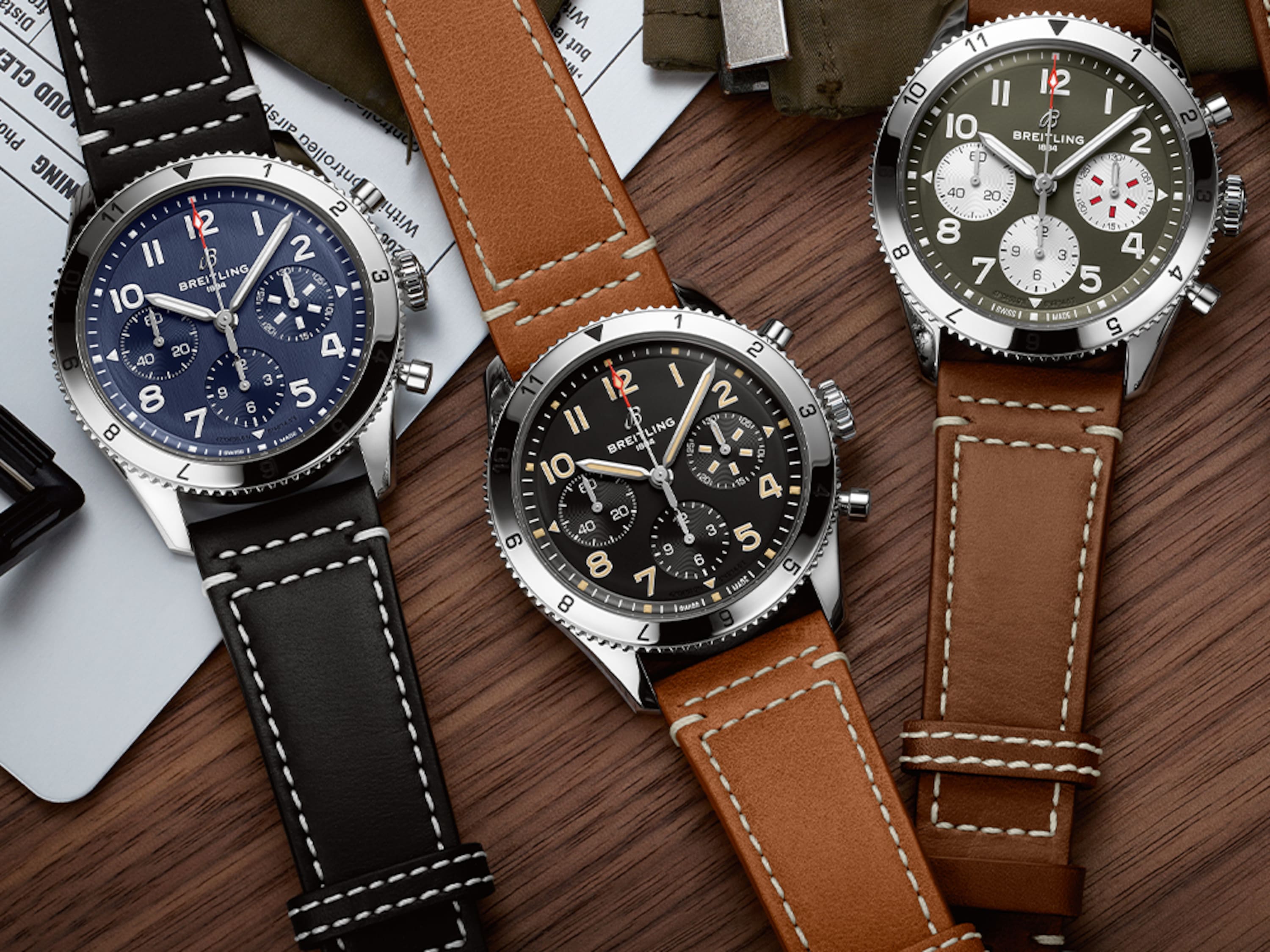 三張 Classic AVI 搭配不同顏色的深色皮革表帶,放在深棕色的桌子上。