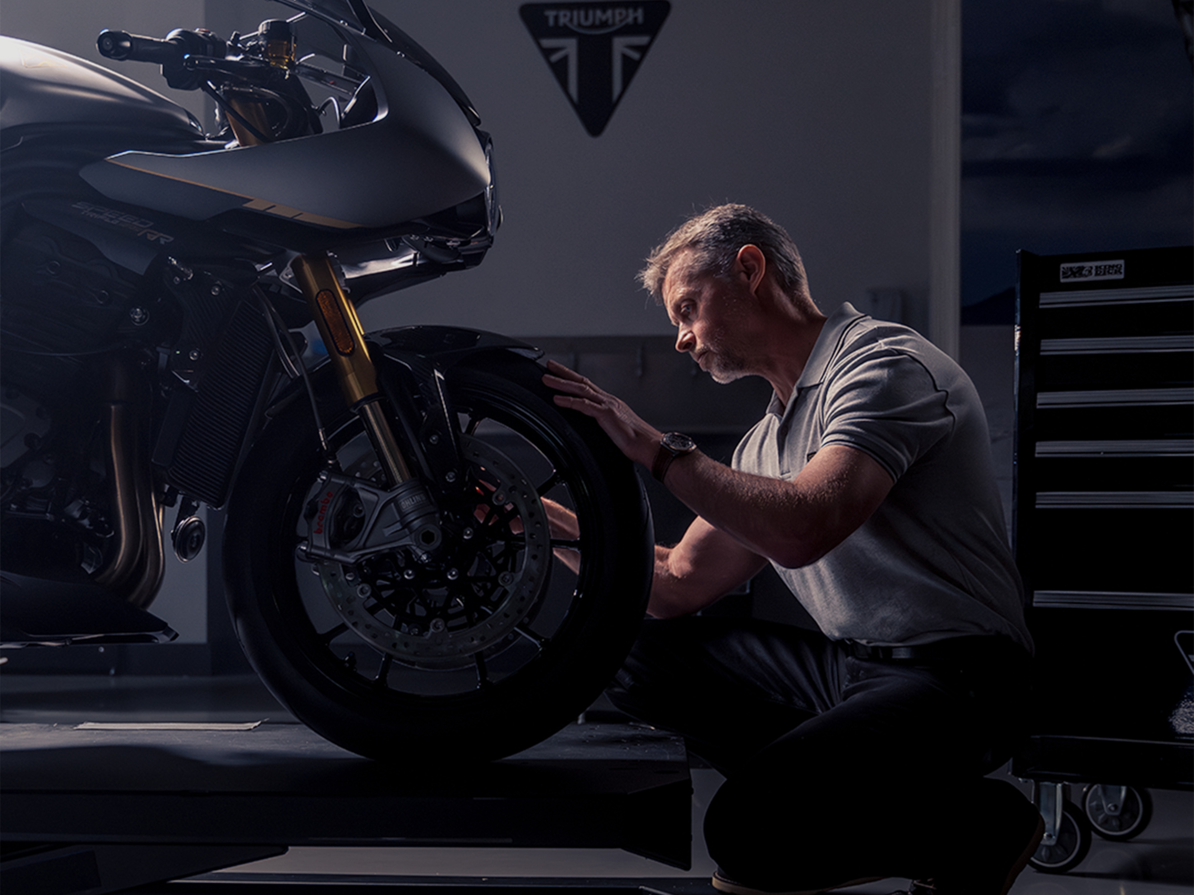 對焦 Breitling 腕錶的男子跪在 Triumph 摩托車前